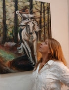 Artist Ingela Johansson standing beside her original painting ‘Power,’ featuring a woman riding a white horse through a forest, symbolizing strength and movement.